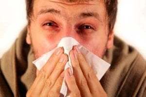 Man sneezing with tissue due to allergy to dust causing red eyes and stuffy nose