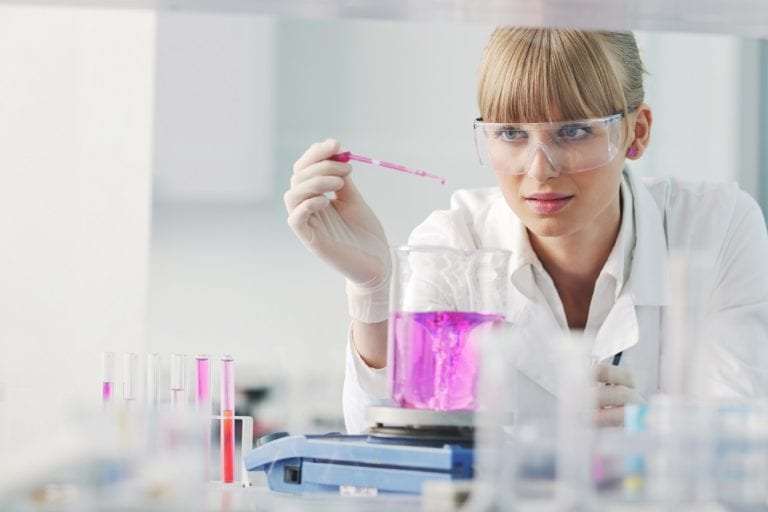 Female scientist in lab coat and safety glasses conducting experiment with pink liquid in beaker, research on eating disorders