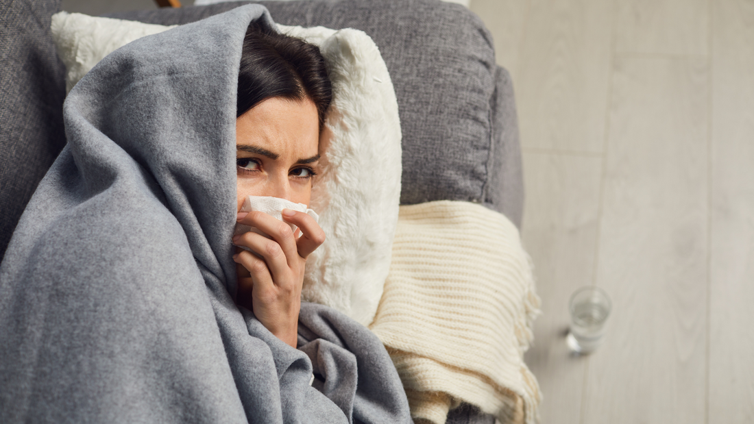 Woman wrapped in blanket blowing her nose, depicting bird flu symptoms and illness concept